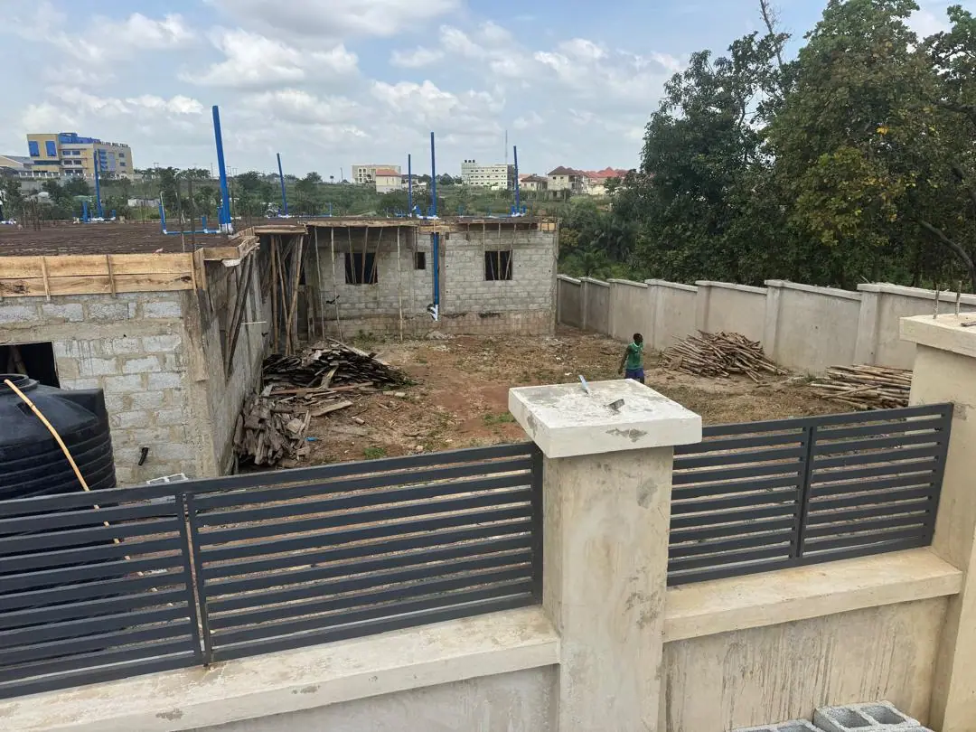 A bungalow at blockwork stage behind a finished fence and slatted gate