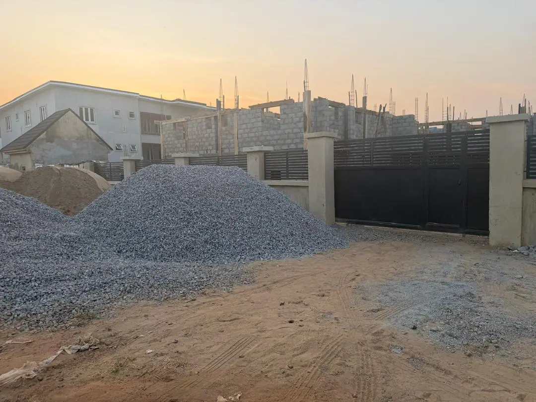 A heap of aggregate inside a walled site beside a charcoal gate at dusk